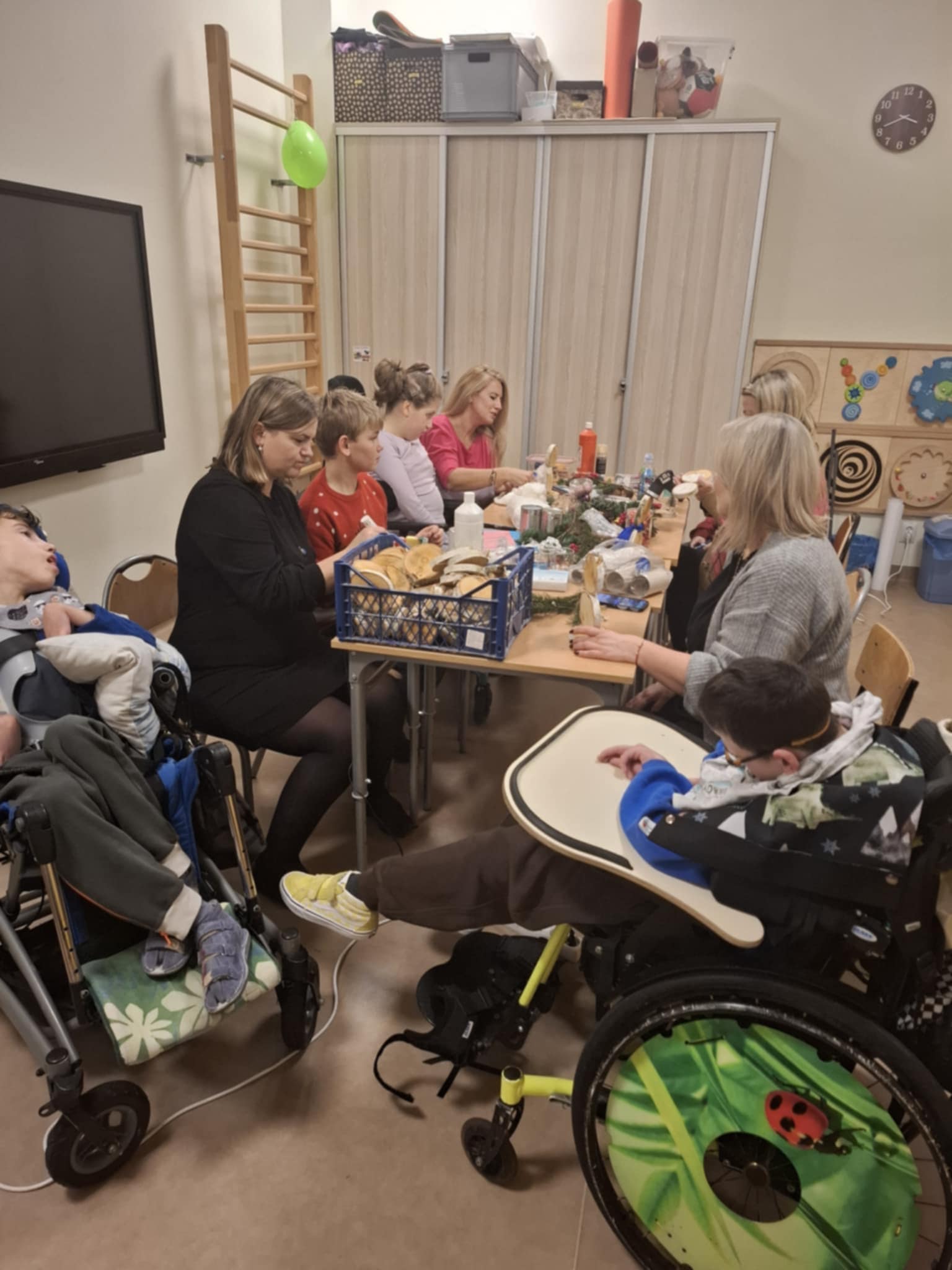 Uczestnicy warsztatów siedzą przy stole, oglądają przedmioty, które służą do wykonania bałwanka.