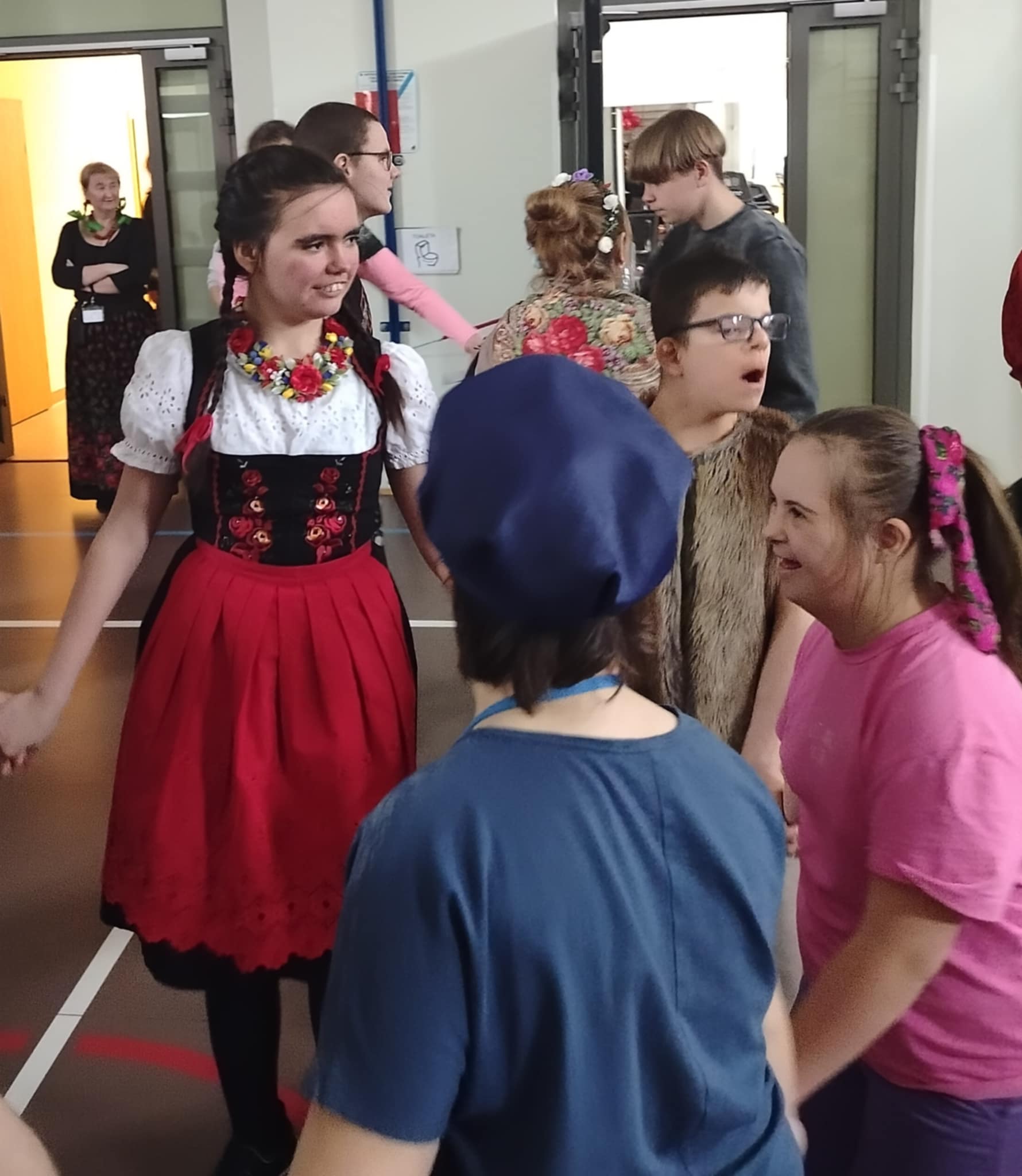 Uśmiechnięte dziewczynki i chłopcy tańczą w kółku trzymając się za ręce. 