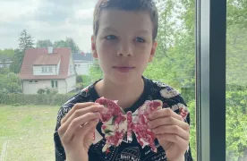Chłopiec w czarnej koszulce trzyma w ręku drewnianego motyla wyklejonego różowo białą serwetką.