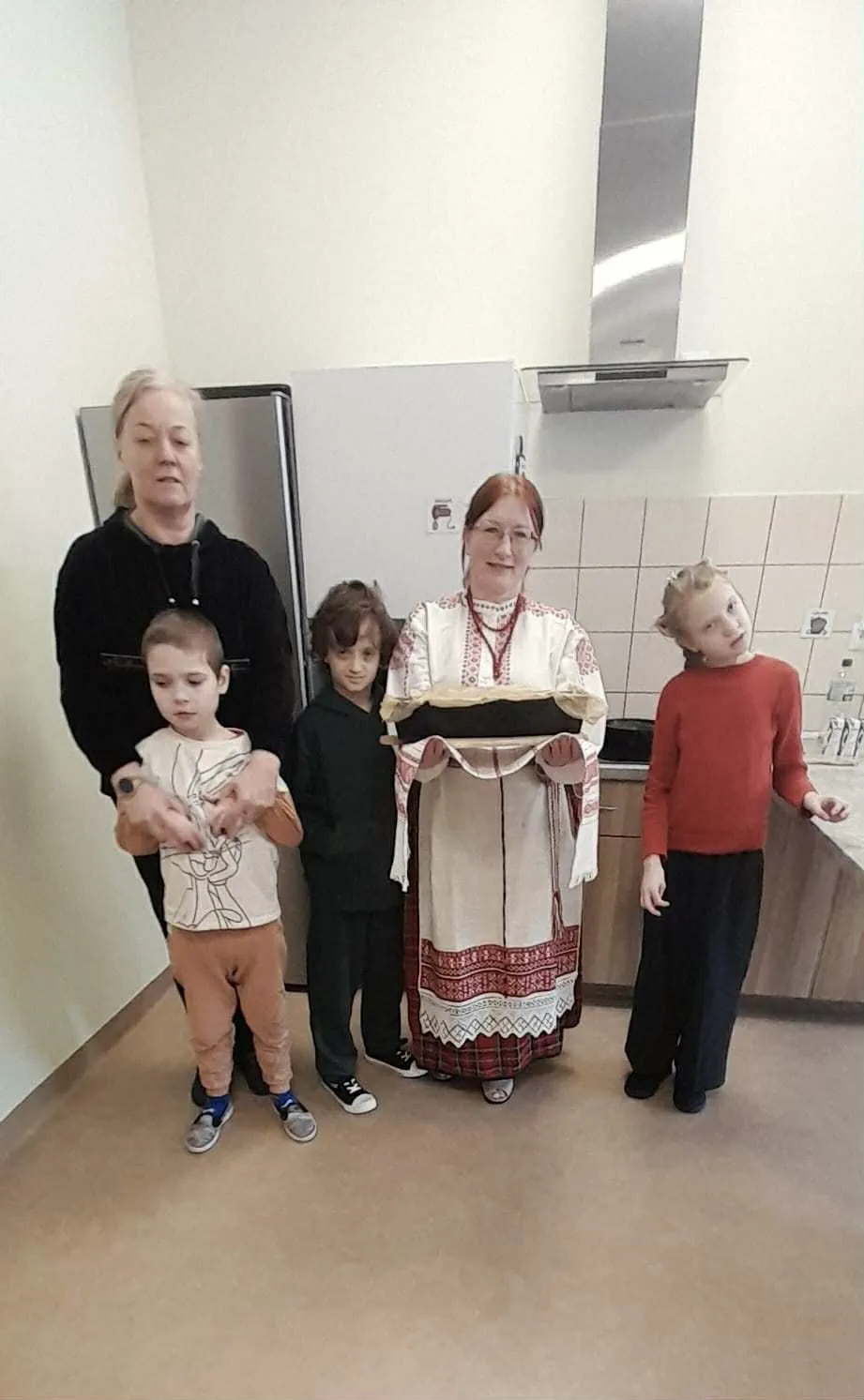 Pani w białoruskim stroju ludowym i uczniowie prezentują upieczoną babkę ziemniaczaną